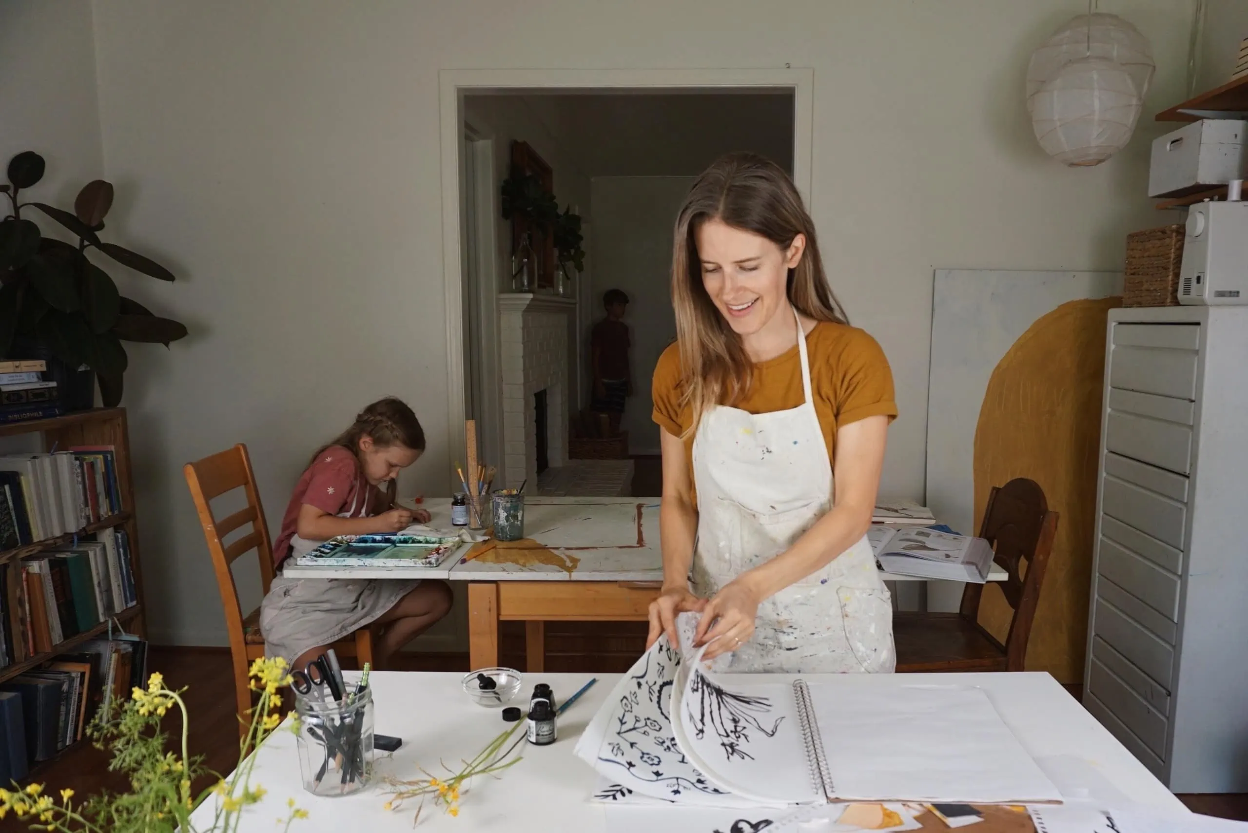 Rachel Smith works on a project. In the background, her daughter draws at a table.