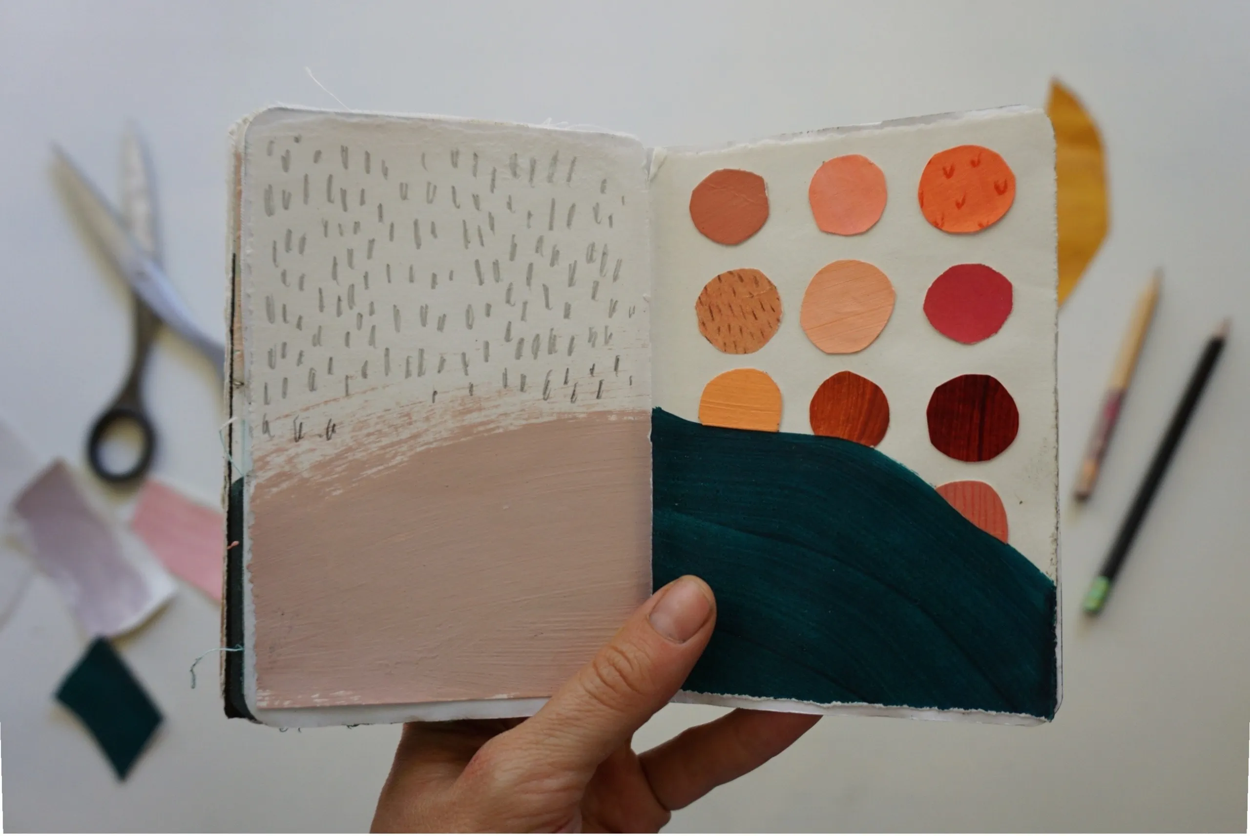 Rachel shows an open view of her sketchbook with painted and collaged shapes, as well as pencil-drawn marks.