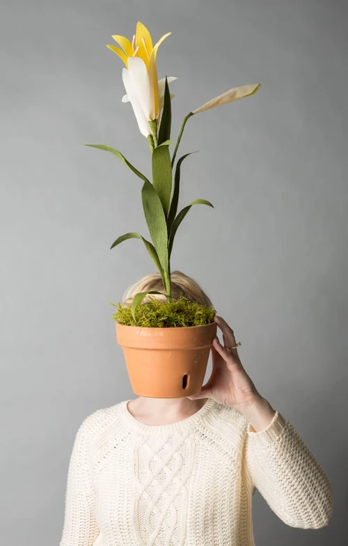 Brittany holds a paper easter lily in a terracotta pot in front of her face