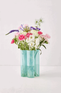 Pink, purple and white flowers burst out of a scalloped aqua vase