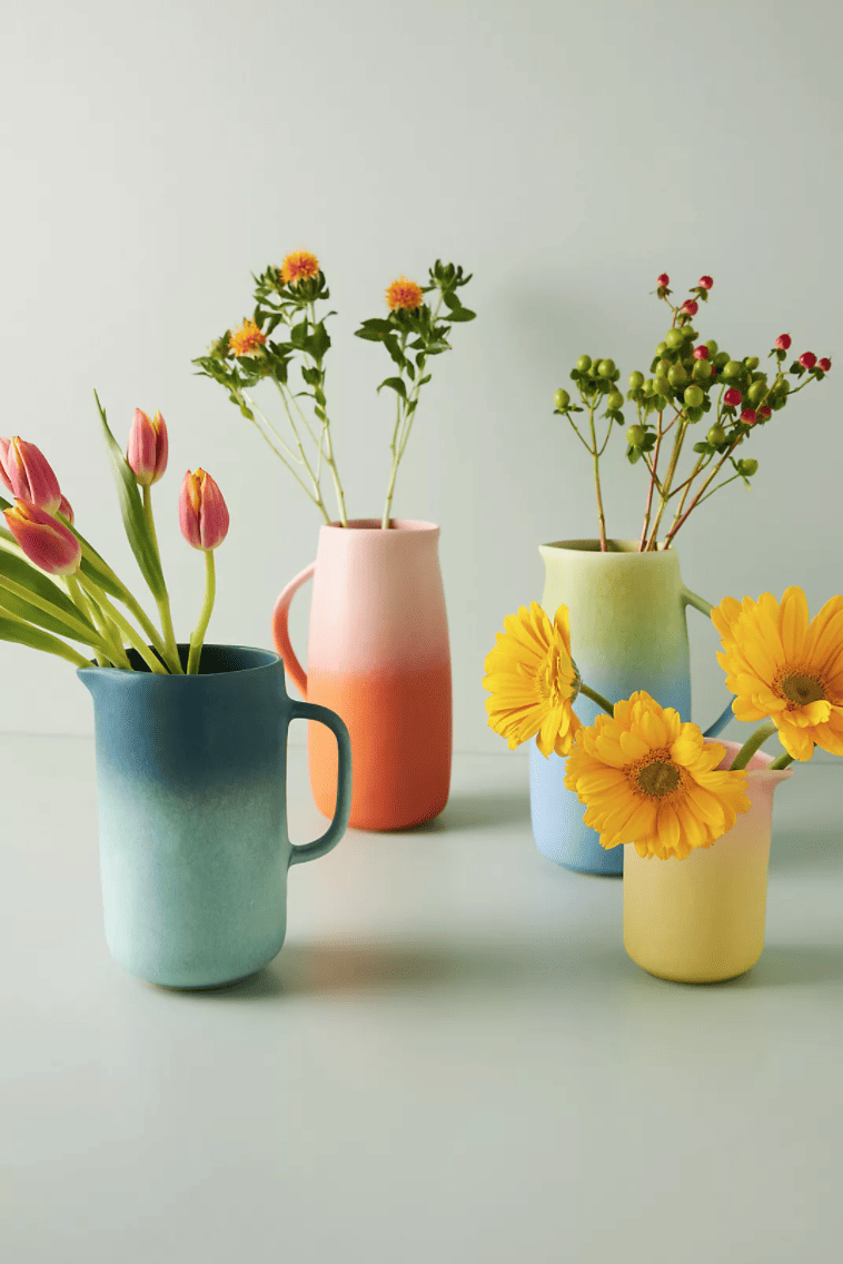 Fresh flowers in warm colors stick out of blue, pink, yellow, and aqua two-toned vases