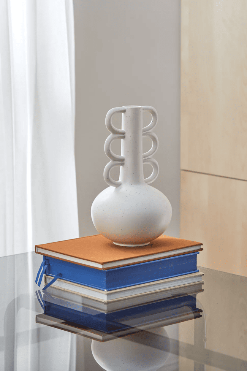 A vase with a tall neck and scalloped handles sits on a pile of books