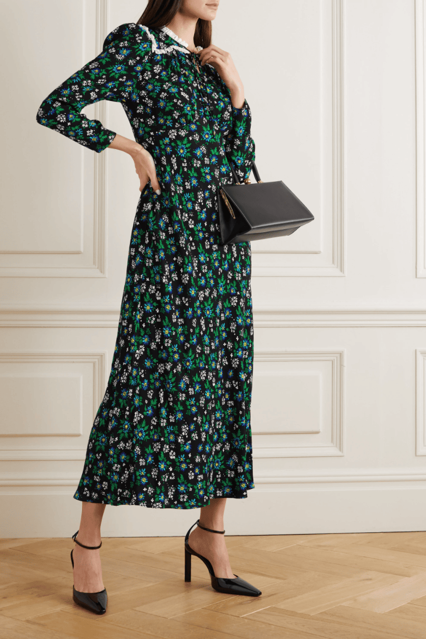 A woman wears a black and green floral printed midi dress with a lace-trimmed collar in a room with light wood floors.