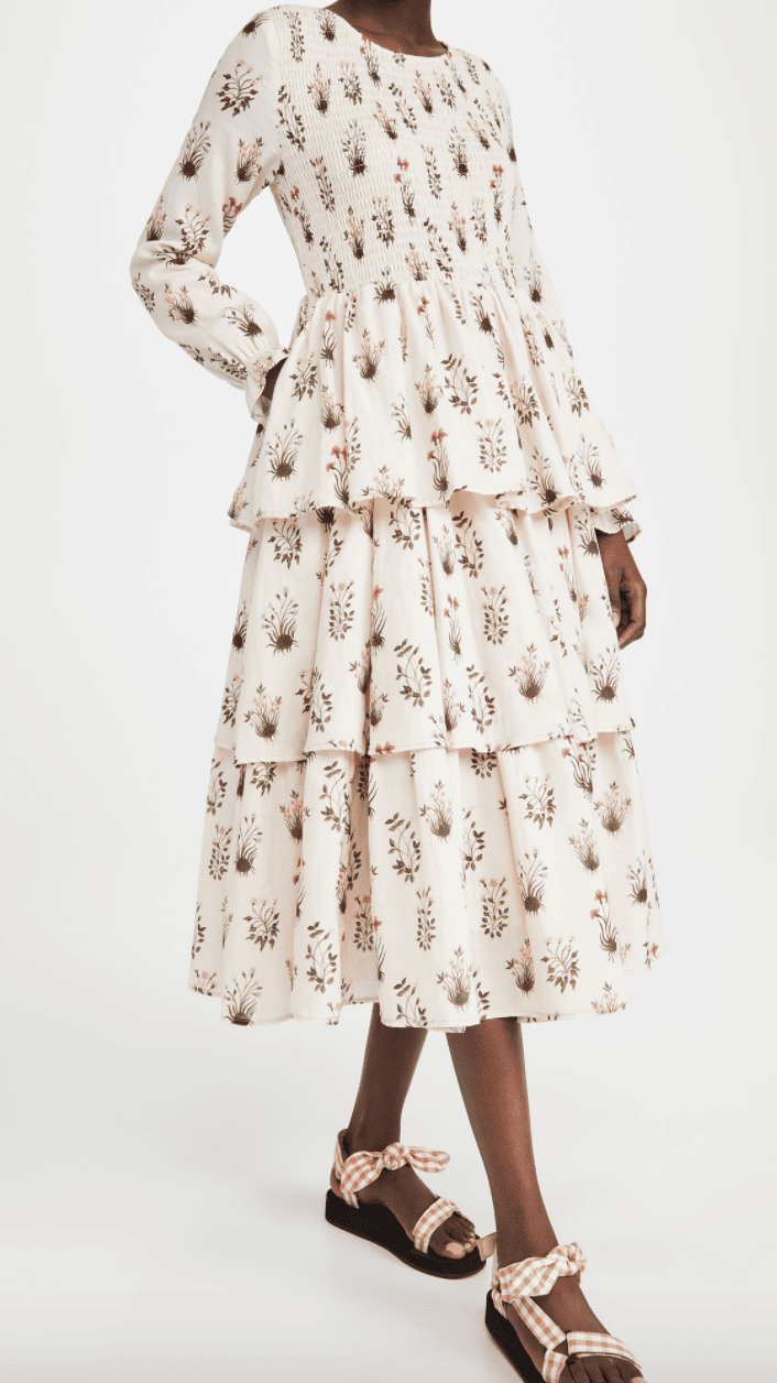 A woman wearing a cream-colored tiered dress with long sleeves and botanical illustrations printed on it.