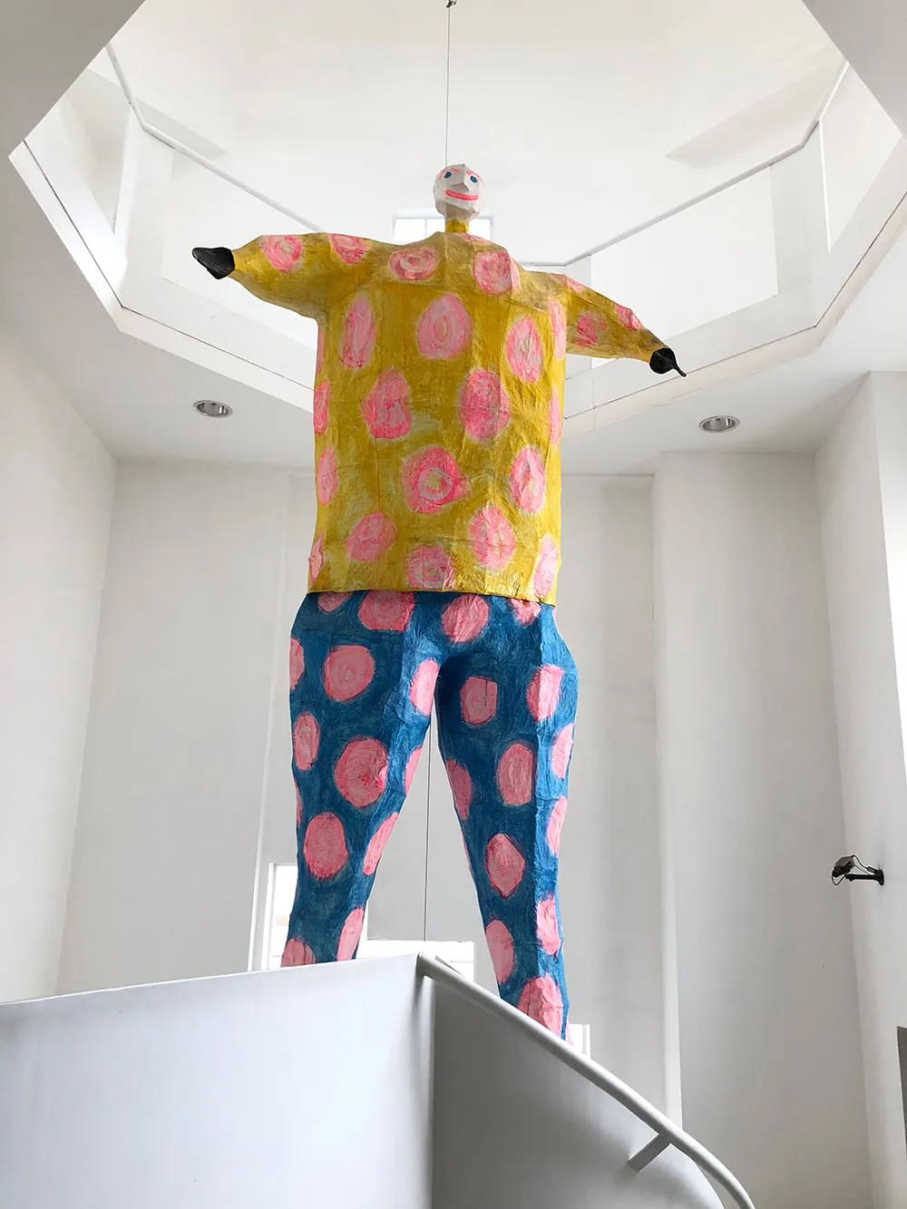 a colorful papier mache man floats in a white museum space 