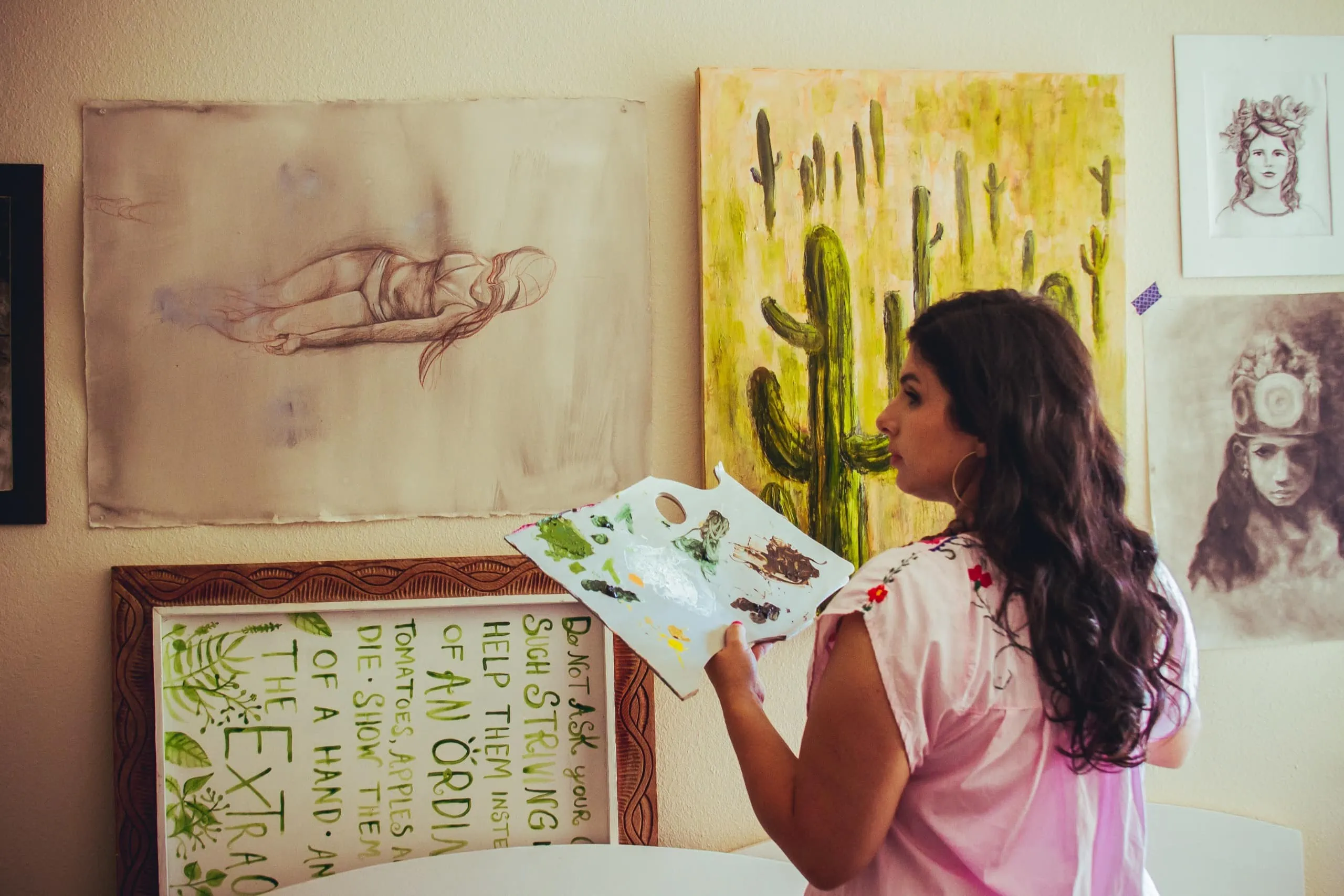 Michelle stands in front of a saguaro painting as well as some other paintings and sketches. 