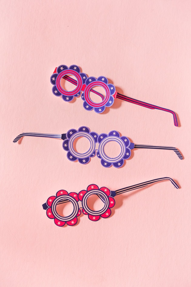 paper glasses with a round floral shape in red and blue with white accents. They're on a blush pink background.