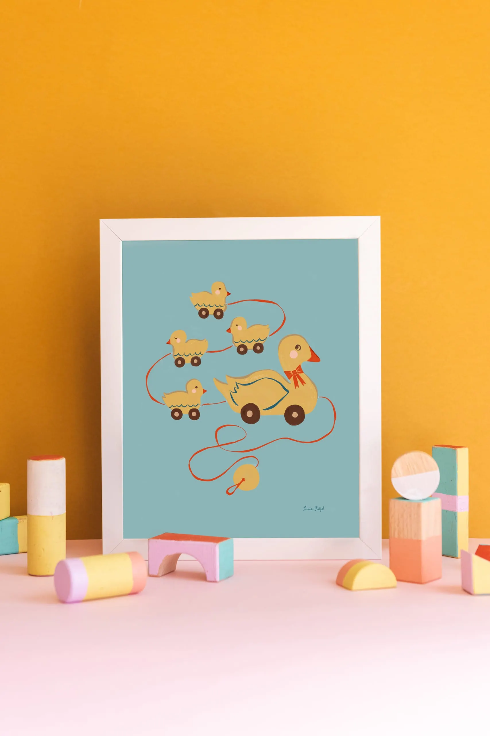 A print of Louise Pretzel's Pull Duck Toy against a gold background. Pastel wooden block toys are arranged in front.