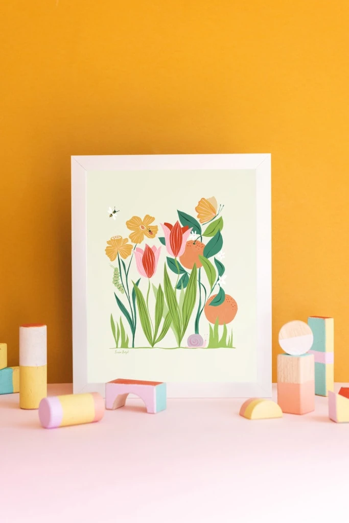 A print of Louise Pretzel's Garden leaning against a gold wall with pastel wooden blocks in front of it.