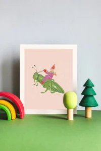 A print of Louise Pretzel's Grasshopper leaning against a light blue wall with wooden rainbow and tree toys in front of it.