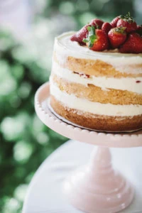 strawberry-covered layer cakes on pastel cakestands at an outdoor party