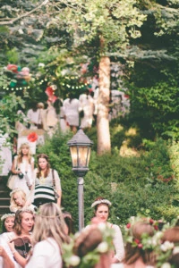 Women dressed in white descend stairs in a green space filled with dappled light.