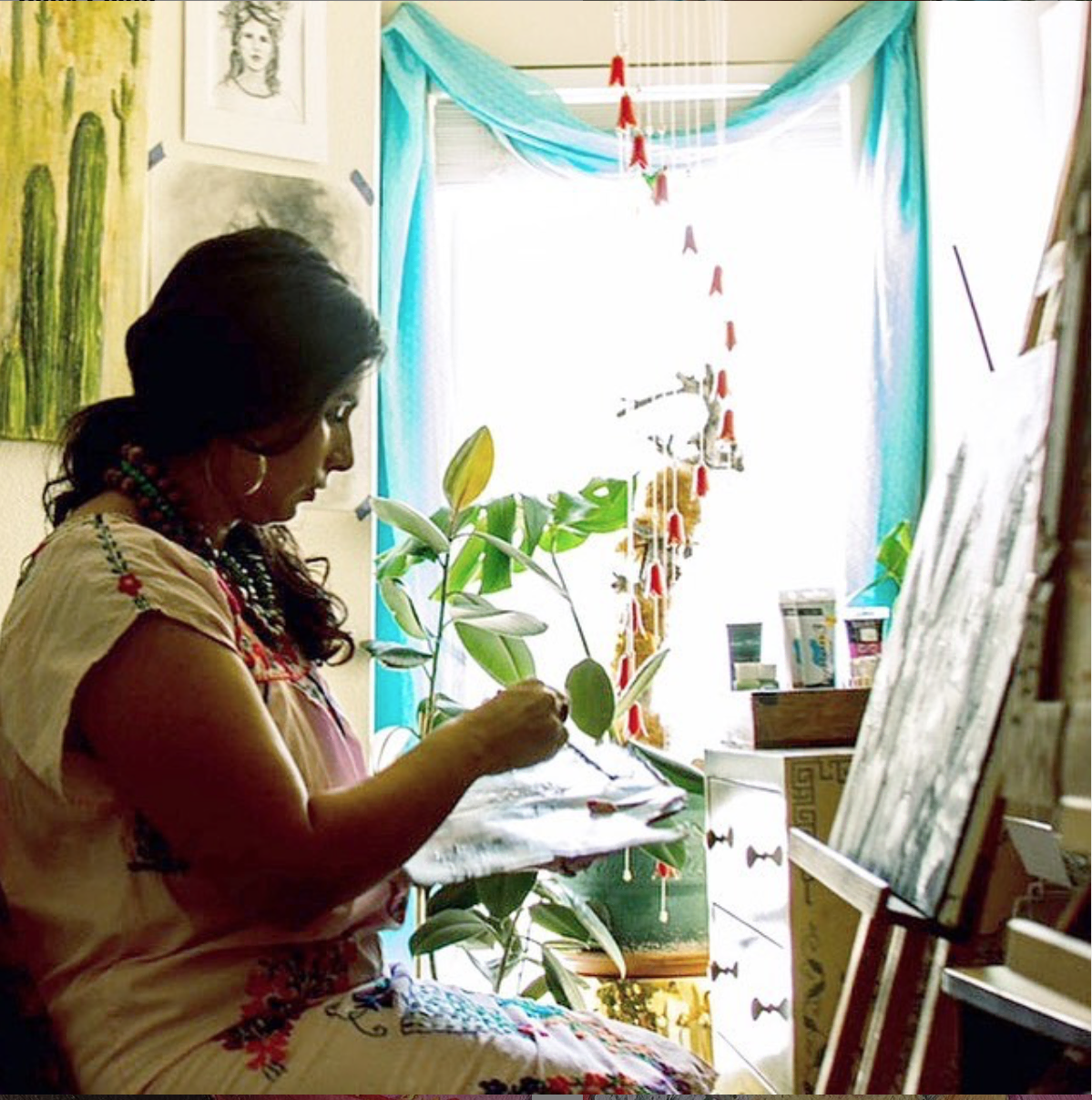 Michelle paints in a light filled room with plants around her. 