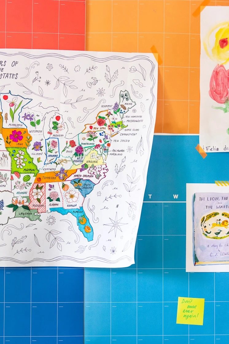 The State Flower Map Coloring Page hangs on Brittany's rainbow calendar with some art prints and a painting by Jasper.