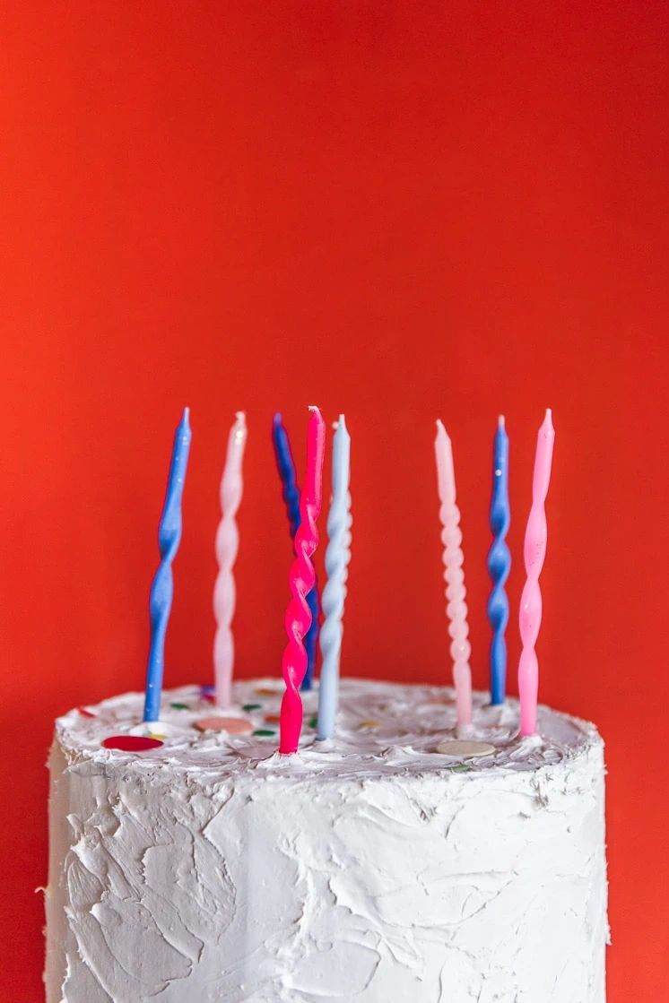 Twisted birthday candles on a white cake with a red background.