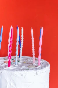 Close up of twisted birthday candles on a white cake with a red background.