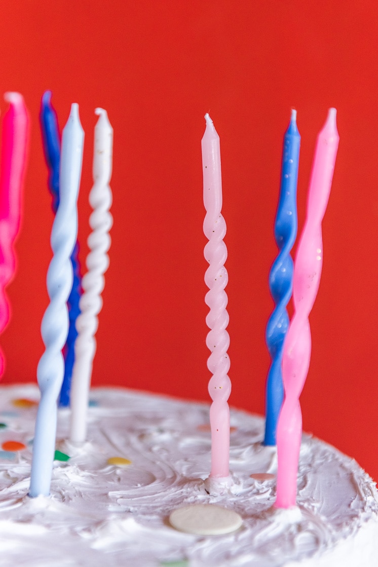 Close up of twisted birthday candles on a white cake with a red background.