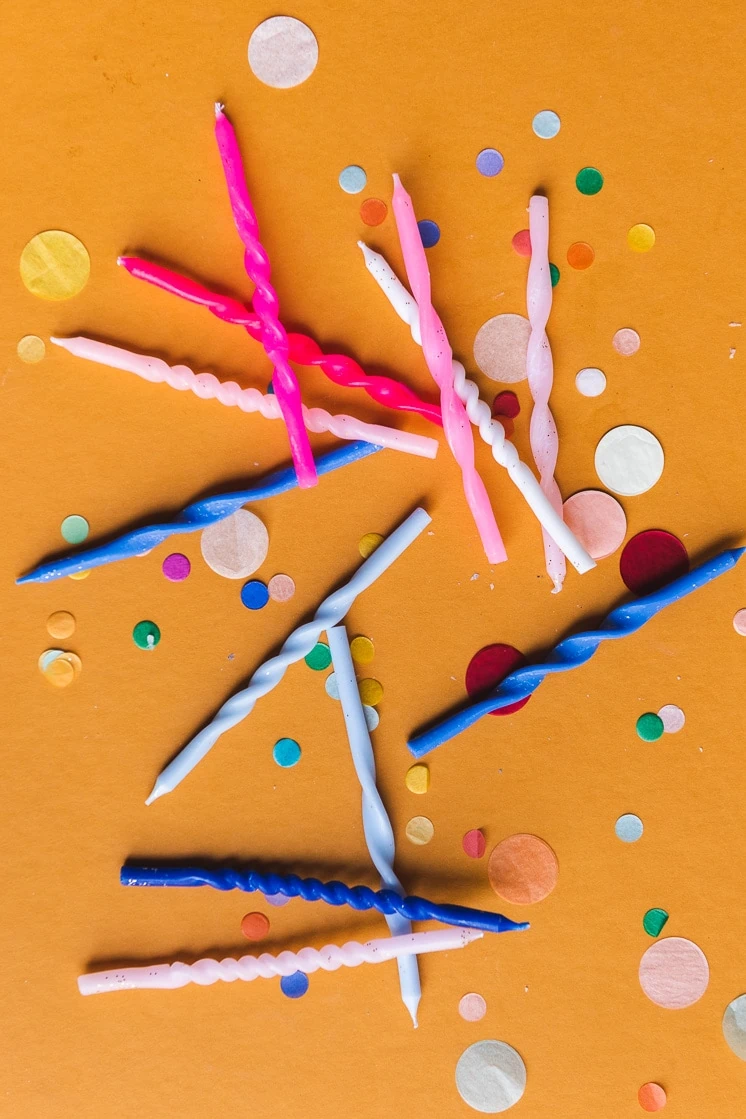 A flat lay of twisted birthday candles and confetti on an orange background.