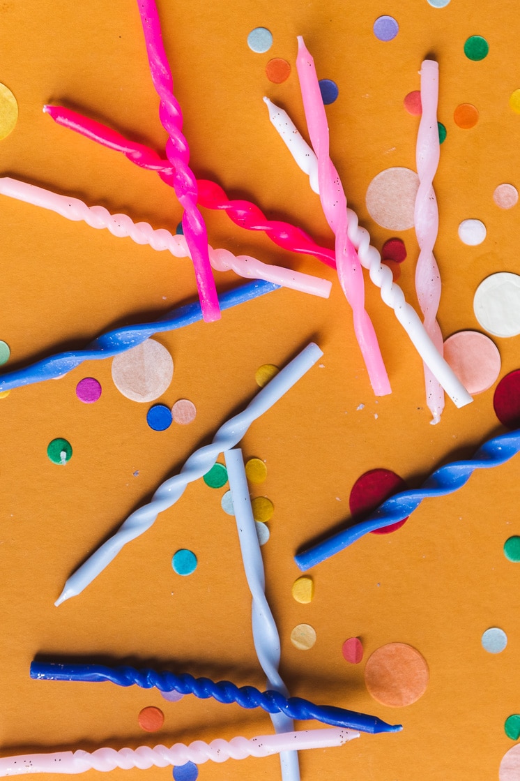 A flat lay of twisted birthday candles and confetti on an orange background.