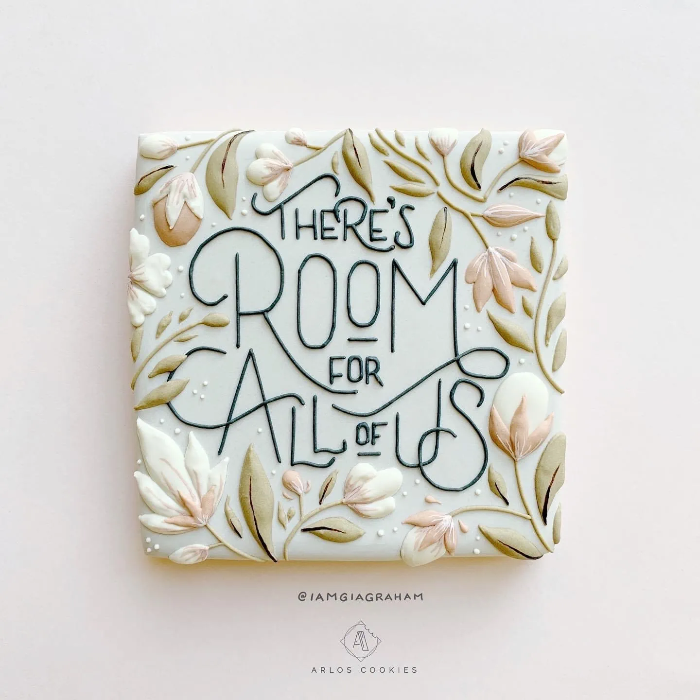A square cookie decorated with pink and green flowers and decorative text reading "there's room for all of us"