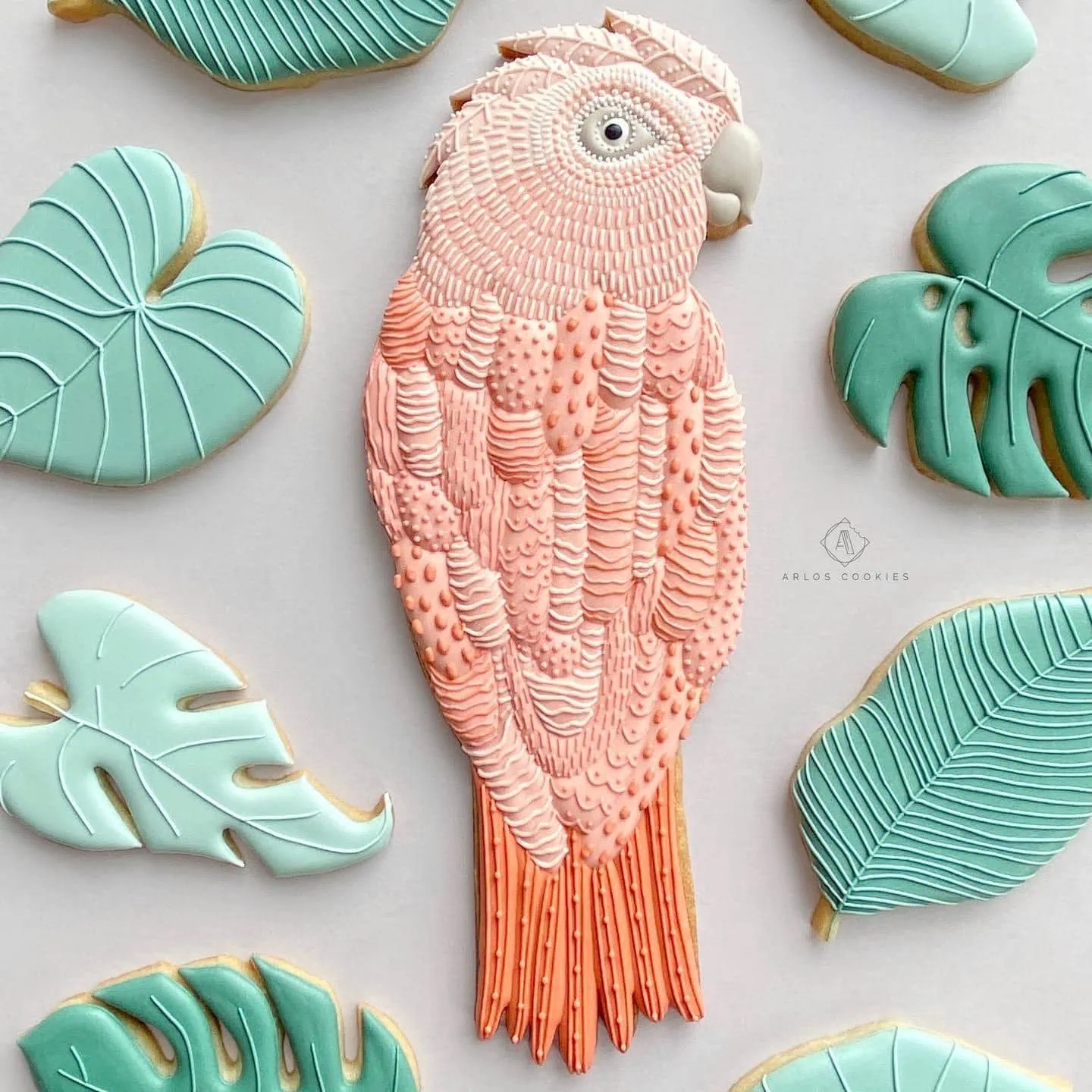 Decorated pink parrot cookie surrounded by green leaf cookies.