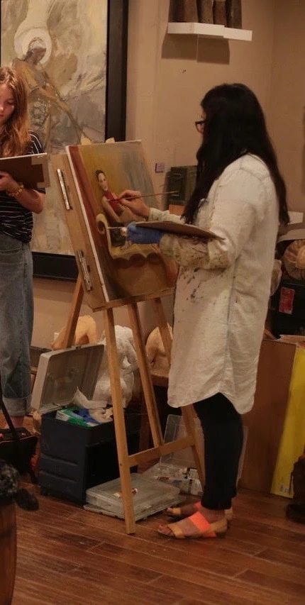 Michelle stands in a dim room painting at an easel. 