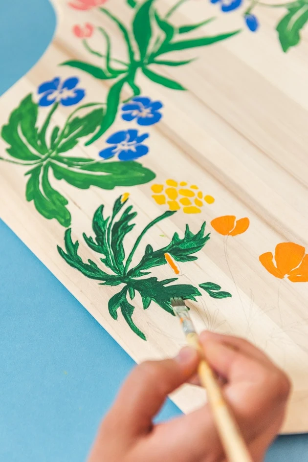 painting a leaf onto a decorative floral painted pizza peel/charcuterie board.