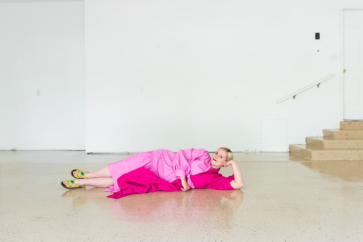 Brittany lies down on the epoxy floor wearing a two-toned pink dress.