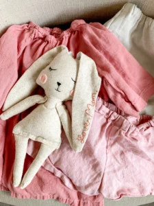 A handmade rabbit doll on top of pink kid's clothes.