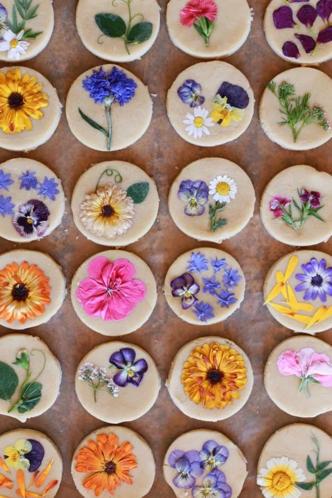 Brightly colored flowers pressed onto sugar cookies on a wooden background.