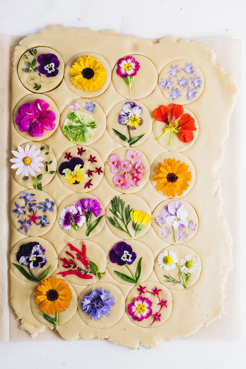 Brightly colored flowers pressed and baked onto sugar cookies on a wooden background.