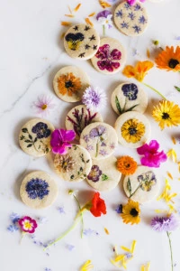 Brightly colored flowers pressed and baked onto sugar cookies on a marble background