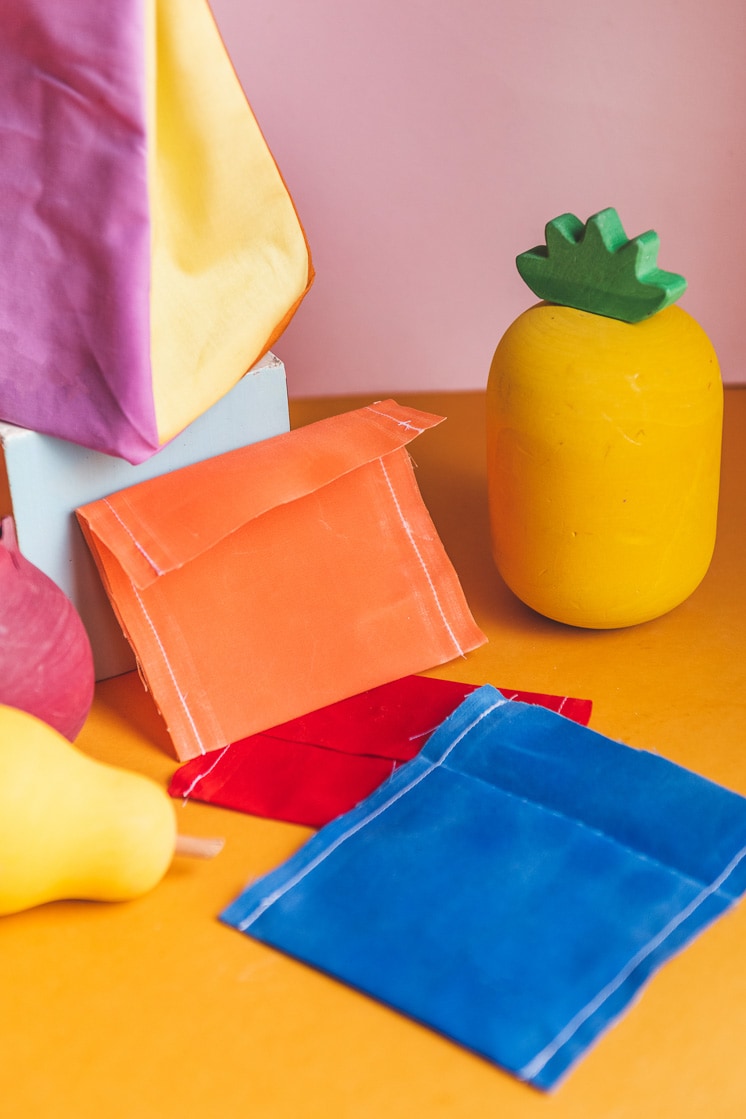 Colorblocked lunch sacks and beeswax snack wraps surrounded by play fruit.
