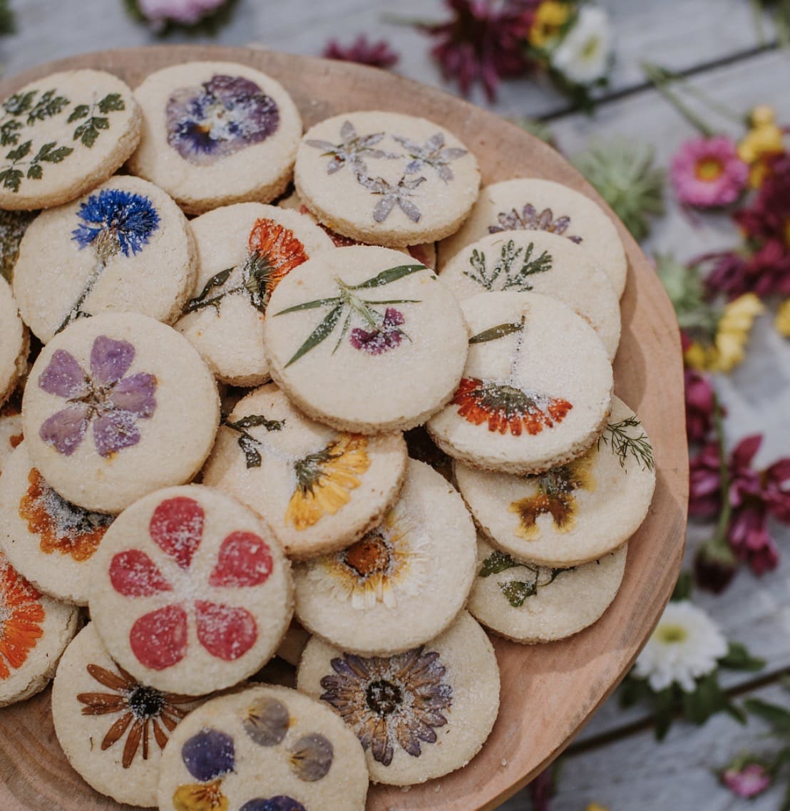 Brightly colored flowers pressed and baked onto sugar cookies on a wooden background.