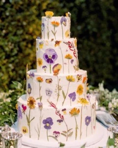 Tall wedding cake frosted with white frosting and purple and yellow flowers