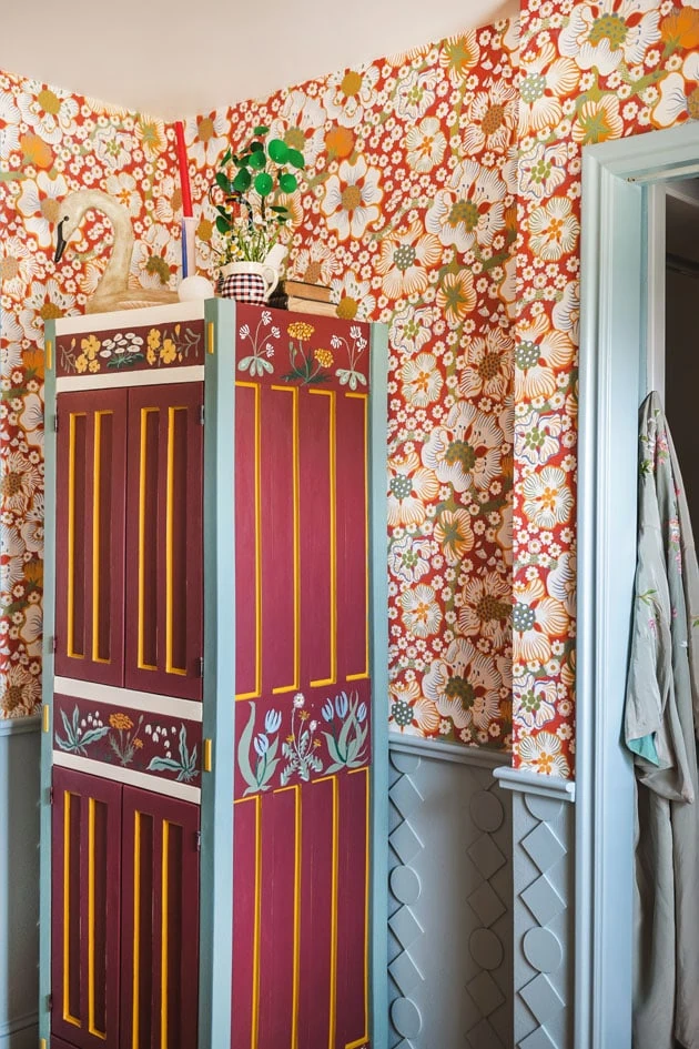 Interior shot of a custom painted cupboard and blue DIY wainscoting in a red floral bathroom.