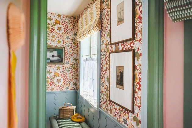 Interior shot of the red wallpapered bathroom from inside a pink and green painted closet. 