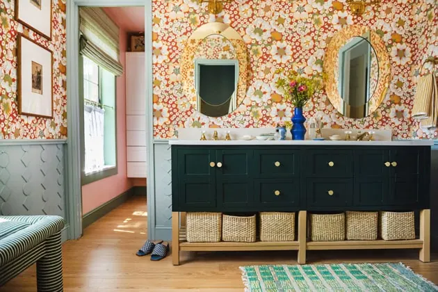 Horizontal interior shot of a bathroom with red floral wallpaper, a green vanity with brass knobs, and blue diy wainscoting.