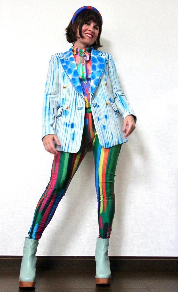 Katie Kortman wearing rainbow striped pants, blue boots, and a blue blazer with lines and dots. 