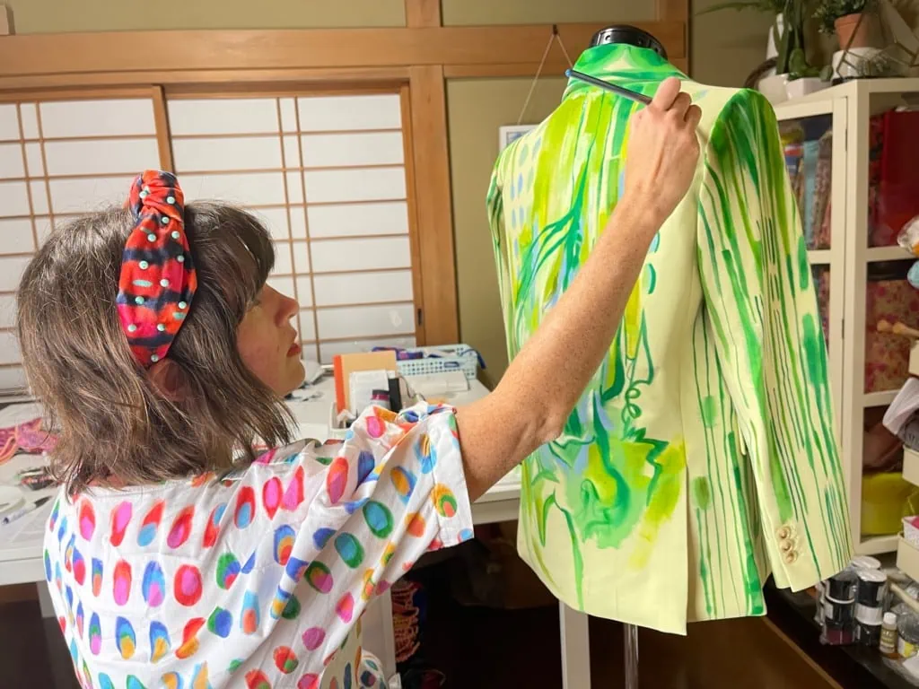 Katie stands by a dress model working on a green blazer design. 