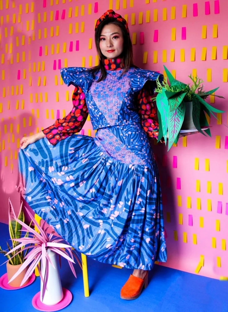 A woman models one of Katie Kortman's designs – a blue and purple dress– while holding a plant.
