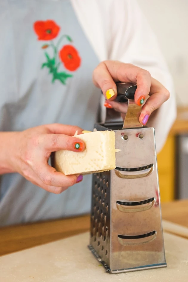 Brittany grates cheese while wearing a light blue apron with red poppies.
