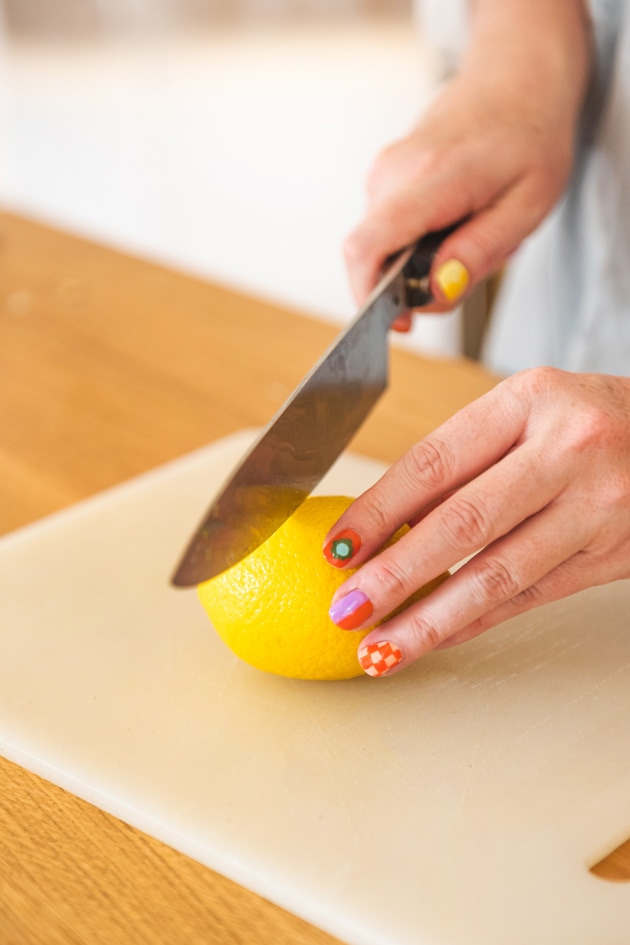 Brittany cuts a lemon open. Her fingernails are painted spectacularly with checkers, flowers, and lines. 