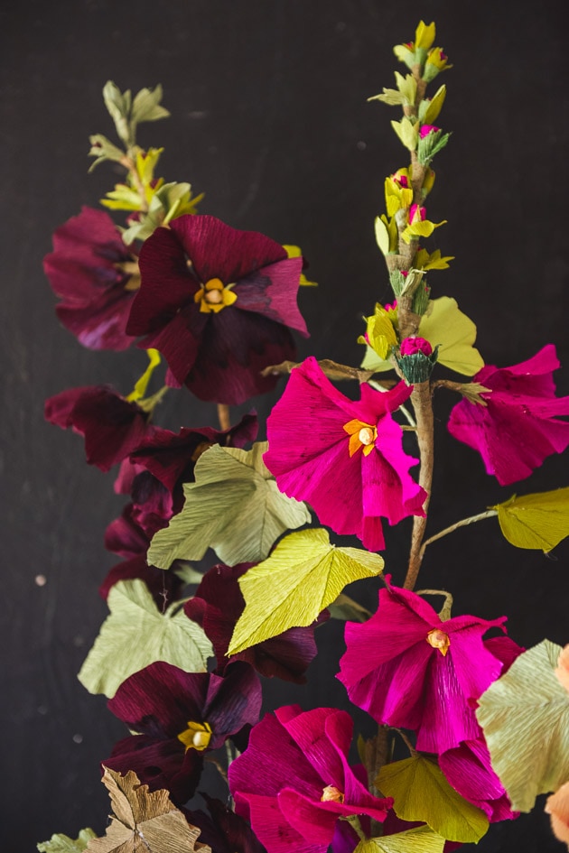 Magenta and purple hollyhocks made of crepe paper against a dark grey background