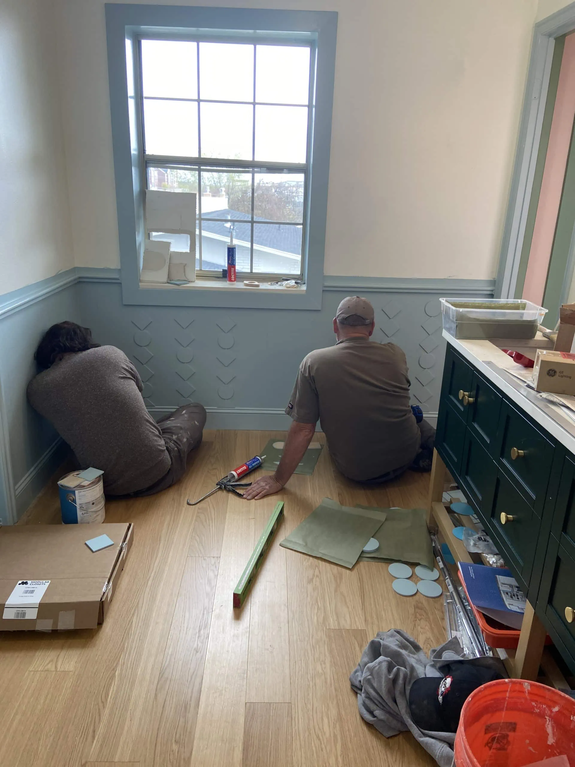 Two workmen glue up wooden cutouts as a custom DIY wainscoting.