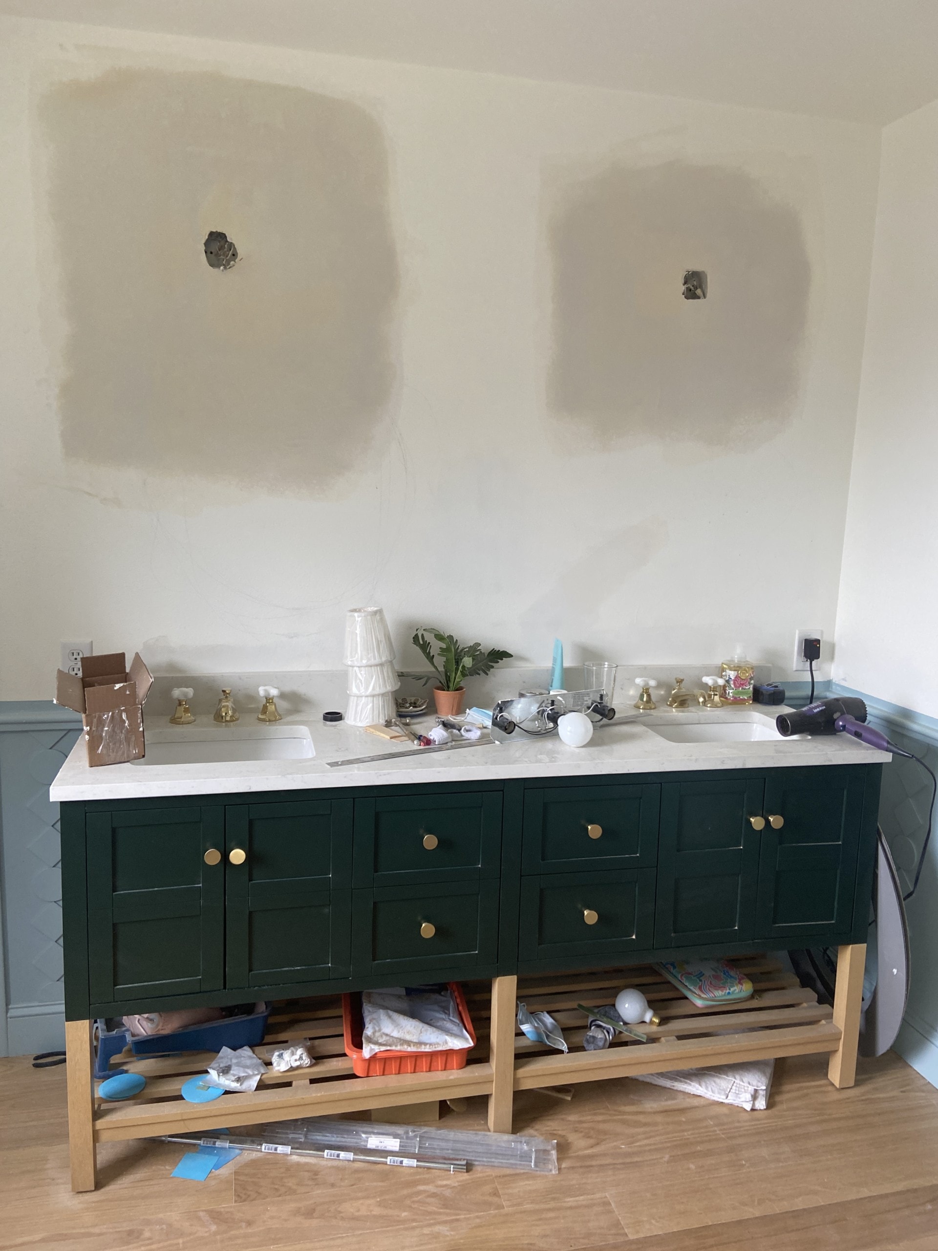 Emerald green vanity with clutter around and on it. The walls are mostly painted white, but are very unfinished.