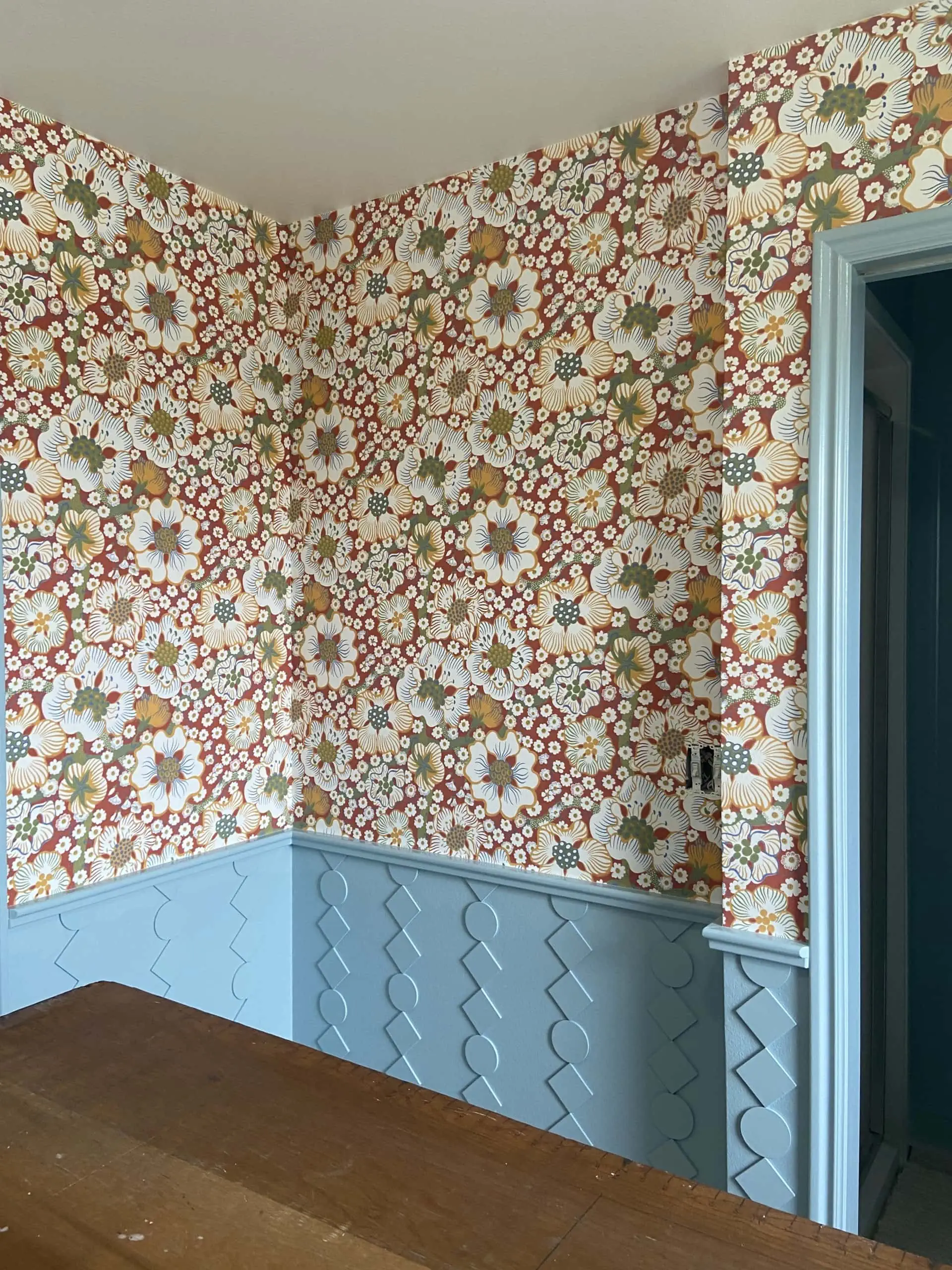 Interior shot of a room with red floral wallpaper and blue custom wainscoting.