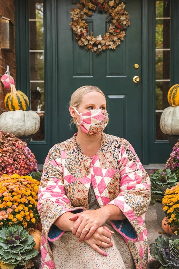 Brittany sitting on her autumn porch wearing a quilted face mask and matching quilted coat.