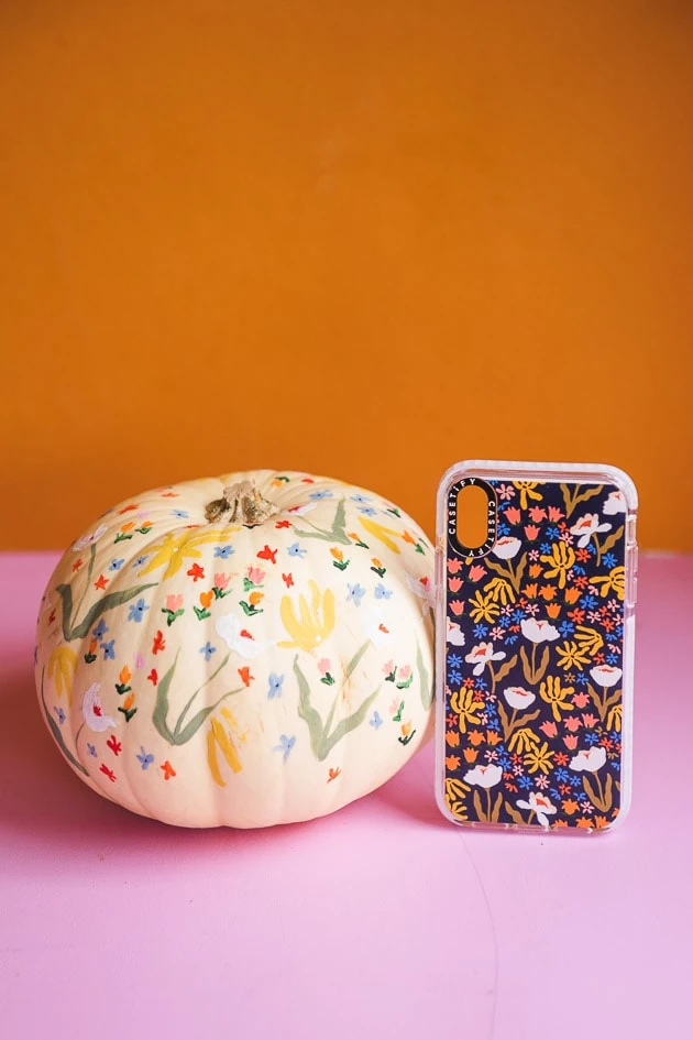 delicate floral painted pumpkin on a pink and orange background. There's a matching phone case next to it.