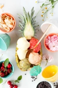 pineapple cut in half filled with scoops of sorbet surrounded by bright colorful cups and flowers